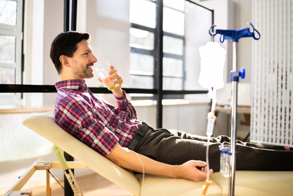 A man getting IV therapy and drinking a glass of water