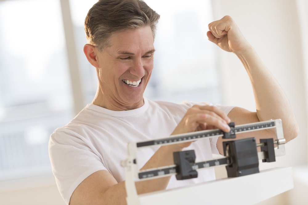 A man standing on the scale and celebrating weight loss after taking Tesofensine A man standing on the scale and celebrating weight loss after taking Tesofensine