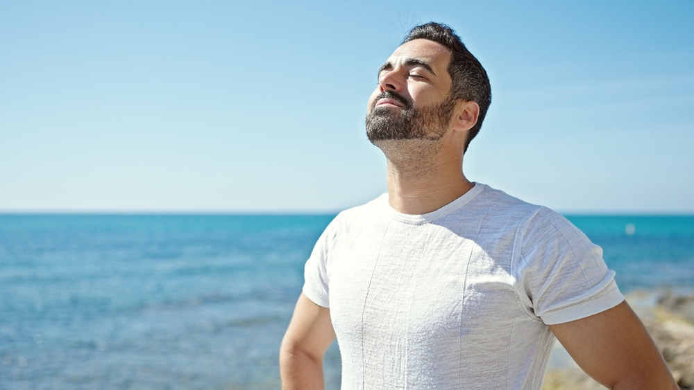 Man standing by the ocean taking a deep breath, representing men’s health, energy, and wellness.